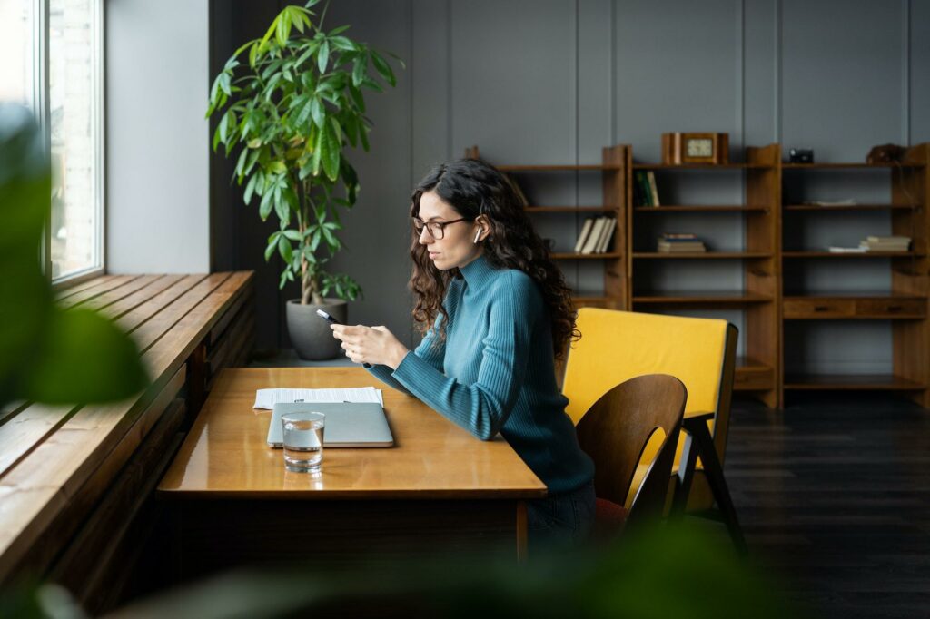 Woman copywriter freelancer using smartphone to check social media at workplace working remotely